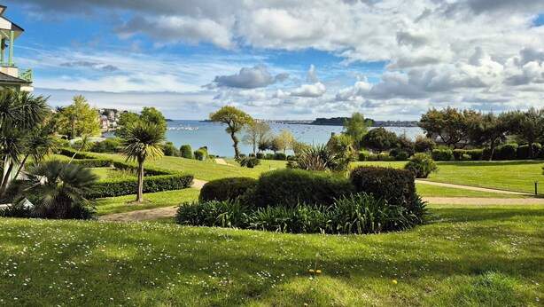 A park with manicured lawns, a variety of trees, and a body of water in the background. - Nest with beautiful garden and sea view (Dinard)