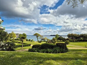 Un parco con prati curati, diversi alberi e una distesa d'acqua sullo sfondo.