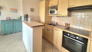 A compact kitchen with wooden cabinets, a microwave, a sink, and an oven. - Nest with beautiful garden and sea view (Dinard)