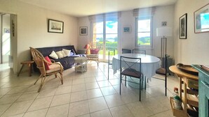 A spacious living room with a sofa, chairs, a dining table, and a view through large windows. - Nest with beautiful garden and sea view (Dinard)
