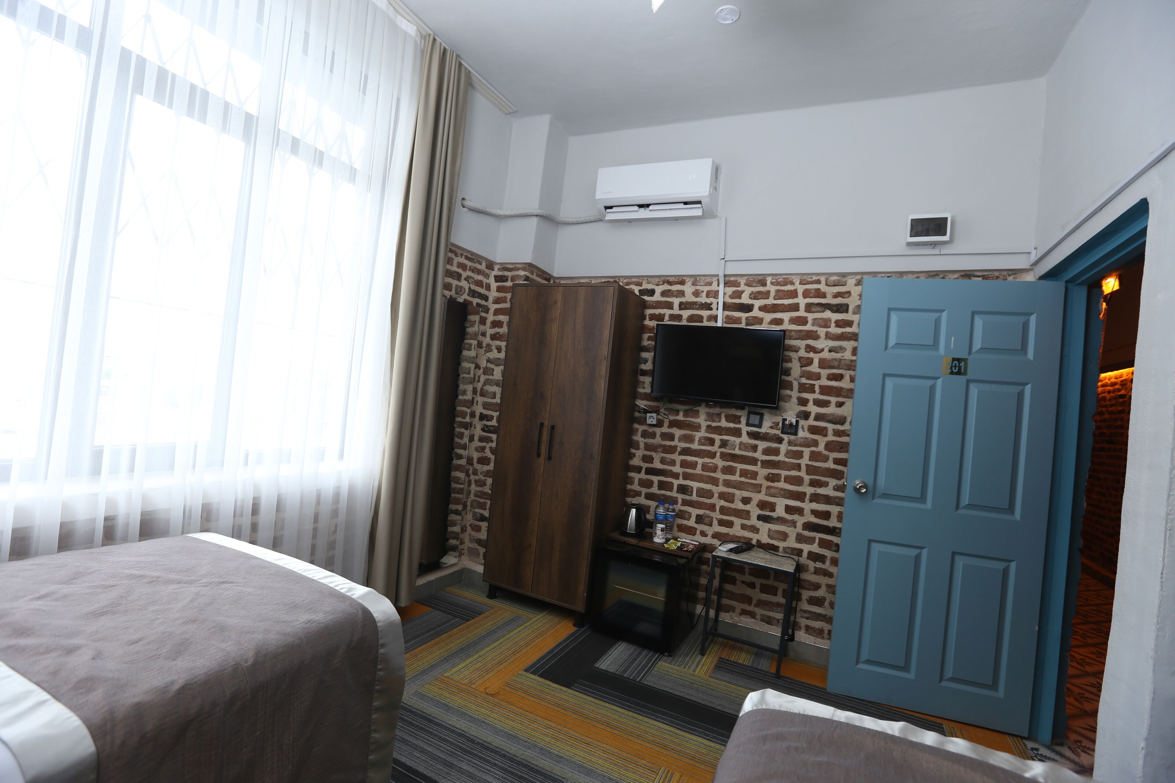 A hotel room with a brick wall, a blue door, a television, a small table, and two beds.
