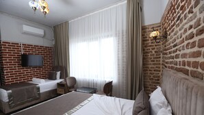 A hotel room with a brick wall, a flat-screen TV, a large bed with white bedding, a desk, and a chair. - Sur Central Hotel (Diyarbakir)