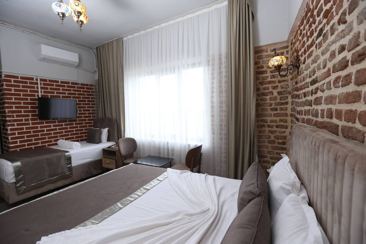 A hotel room with a brick wall, a flat-screen TV, a large bed with white bedding, a desk, and a chair.