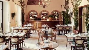 En restaurant med runde borde, fletstole og et barområde med flasker på hylder.