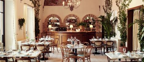 A restaurant with round tables, wicker chairs, and a bar area with shelves of bottles.