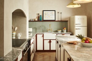 A kitchen with a marble countertop, white cabinets, a white refrigerator, and a fruit bowl.
