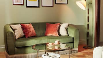 A green sofa with multiple cushions, a glass coffee table with a book and a cup, and a floor lamp.