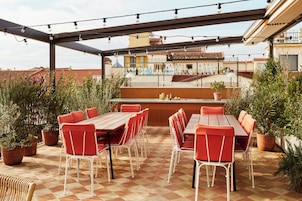 Patio esterno con tavolo di legno e sedie rosse, circondato da piante in vaso.