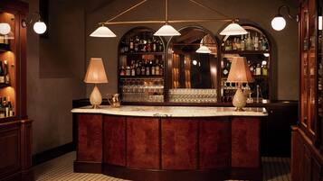 Zona de bar con una barra curva de madera, dos lámparas y un espejo que muestra botellas y vasos.