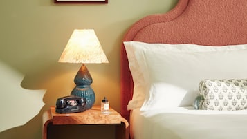 Una cama bien tendida con sábanas blancas y un cabecero rojo, una mesita de noche con una lámpara, y una obra de arte enmarcada sobre la cama.