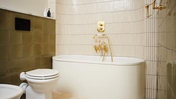 A bathroom with a white bathtub, a white toilet, and a gold showerhead.