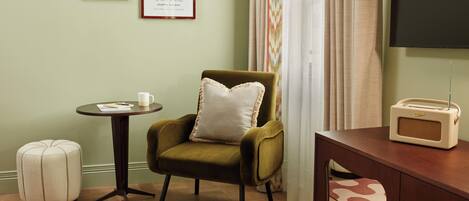 A room with a green armchair, a small round table with a cup and a book, a vintage radio, and two framed pictures on the wall.