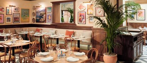 A restaurant with round tables, wooden chairs, and a large potted plant.