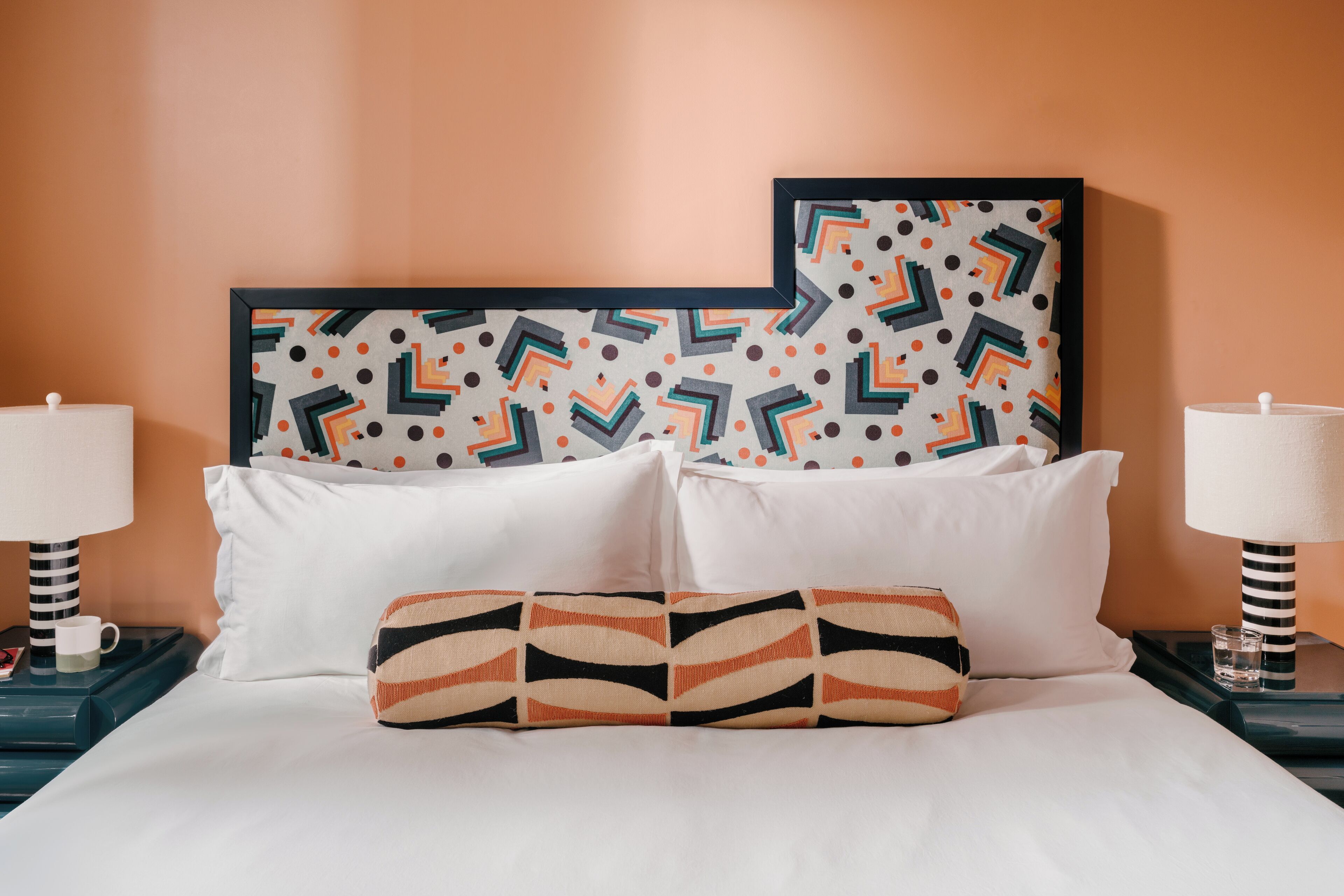A neatly made bed with white linens and a patterned pillow, flanked by two nightstands with lamps and a framed artwork above.