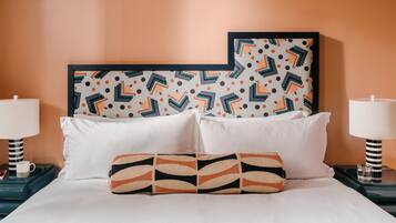 A neatly made bed with white linens and a patterned pillow, flanked by two nightstands with lamps and a framed artwork above.