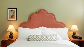 A neatly made bed with white linens, a patterned pillow, and a headboard with a scalloped design. There are two bedside tables with lamps and a framed picture on the wall.