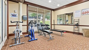 Un gimnasio con equipamiento de ejercicio, una banca y un espejo en la pared.