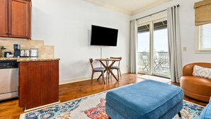 Una cocina moderna con armarios de madera, horno empotrado y cafetera. Hay un comedor con mesa y sillas, y un ventanal con vistas al exterior.