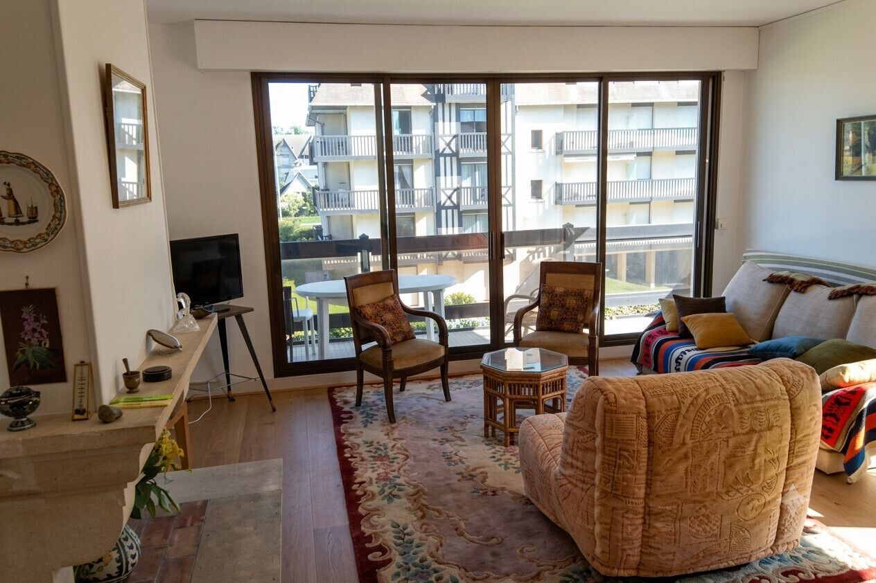 A living room with a sofa, chairs, a TV, a small table, and a balcony with a view of buildings.
