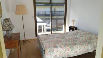 Une chambre avec un lit, un bureau, une chaise, une lampe et une vue sur le balcon extérieur.