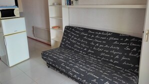 Una habitación compacta con un sofá blanco, un mueble blanco y una estantería blanca con libros y adornos.