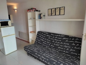A compact room with a white sofa, a white cabinet, and a white shelf with books and decorative items.