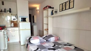 Un dormitorio pequeño con cama, una kitchenette compacta y un armario blanco.