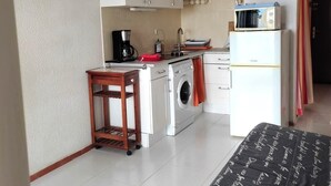 Una cocina compacta con armarios blancos, lavadora, microondas y cafetera.