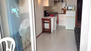 Una cocina compacta con armarios blancos, un pequeño comedor y un ventilador cerca de la ventana.