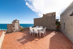 A rooftop terrace with a table and chairs, a view of the sea, and a concrete wall.