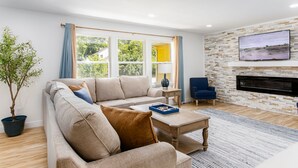 A modern living room with a sofa, a coffee table, a TV mounted on the wall, and a fireplace. - 1 Mile to Notre Dame, Hot Tub, 2400 Sq Ft (South Bend)
