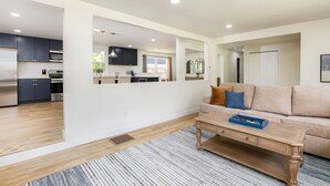 A modern living room with a sofa, coffee table, and a view into the kitchen. - 1 Mile to Notre Dame, Hot Tub, 2400 Sq Ft (South Bend)