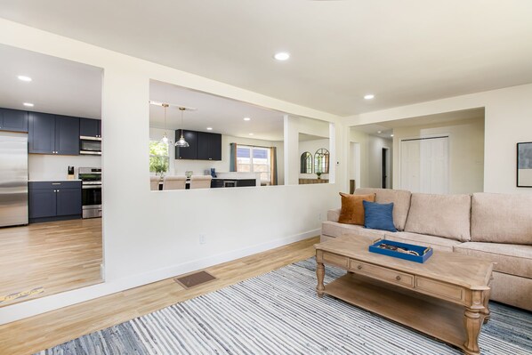 A modern living room with a sofa, coffee table, and a view into the kitchen. - 1 Mile to Notre Dame, Hot Tub, 2400 Sq Ft (South Bend)