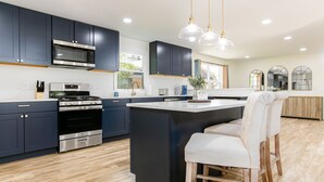 A modern kitchen with dark cabinets, stainless steel appliances, a central island with bar stools, and pendant lighting. - 1 Mile to Notre Dame, Hot Tub, 2400 Sq Ft (South Bend)