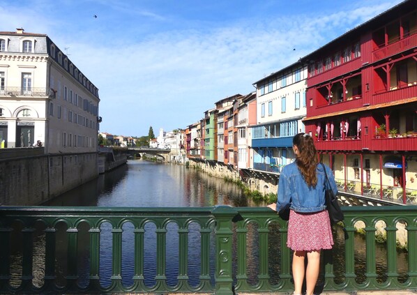 A woman standing on a bridge overlooking a canal with colorful buildings on either side. - Maison Calme et Tranquille Avec Terrasse, Jacuzzi et Climatisation aux Chambres (Castres)