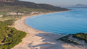 Paisagem costeira com praia de areia, vegetação verde e mar azul límpido.