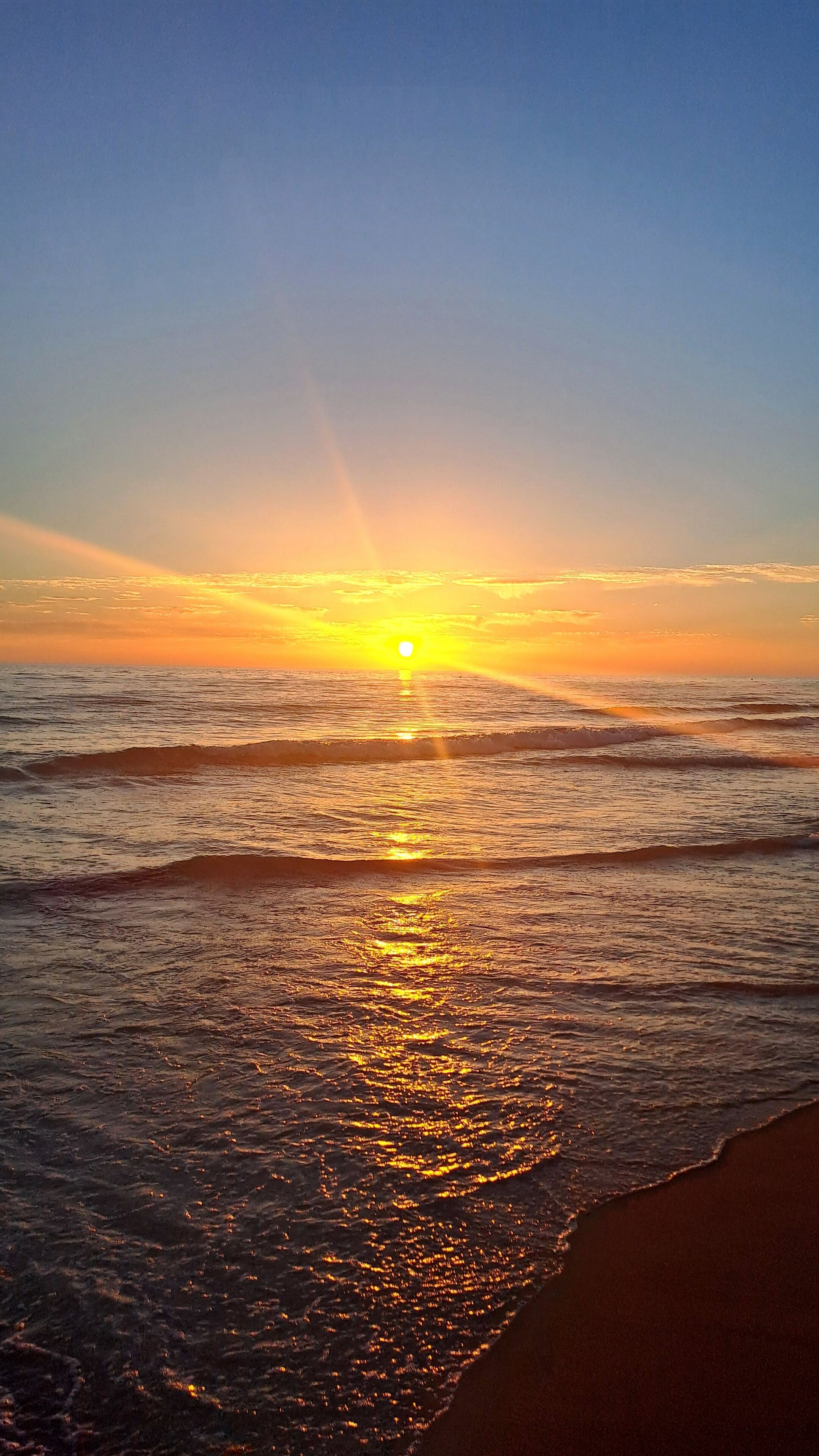 A sunset over the ocean with waves reflecting the sunlight.