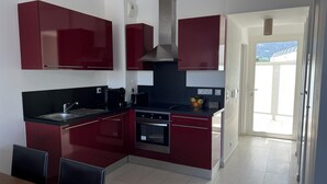 Une cuisine moderne avec des meubles de couleur rouge, un plan de travail noir et un four en acier inoxydable.
