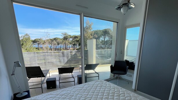 Une chambre moderne avec un grand lit, un balcon avec des chaises et une vue sur des arbres et un immeuble.