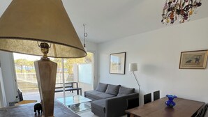 Un salon avec une table en bois, un canapé et une lampe. Il y a une fenêtre donnant sur des arbres.