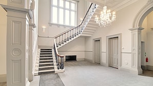 A grand staircase with a black and white balustrade, leading to a landing with a chandelier. - Highfield House (Ripon)