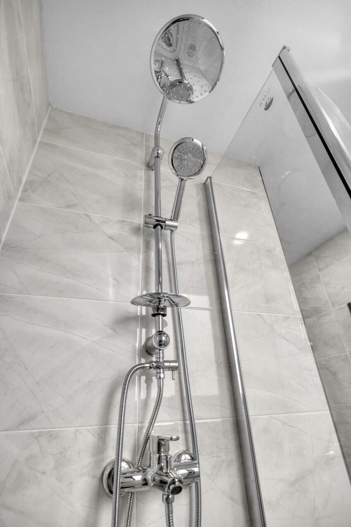 A modern bathroom with a walk-in shower, a handheld showerhead, and a handheld mirror.