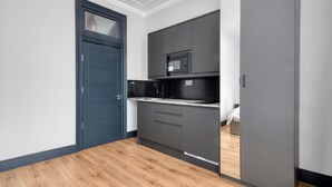 A compact kitchen with grey cabinets, a microwave, and a black refrigerator. - Luxury Studio in London (London)