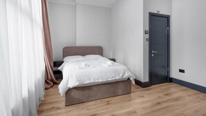 A bedroom with a bed, a nightstand, a door, and a window with curtains. - Luxury Studio in London (London)