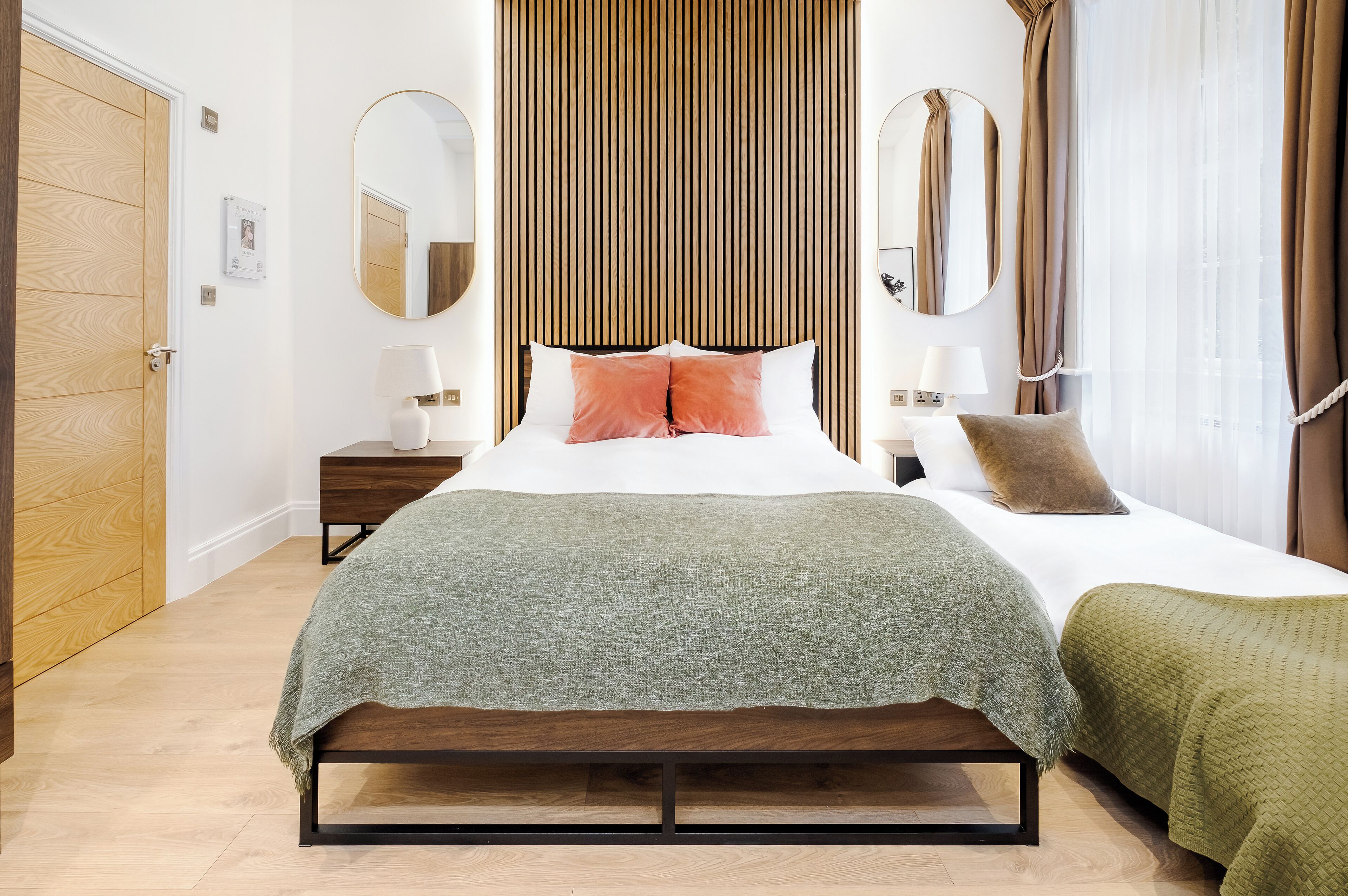 Une chambre à coucher avec un lit en bois, un plaid vert, deux tables de chevet avec des lampes et une armoire en bois.