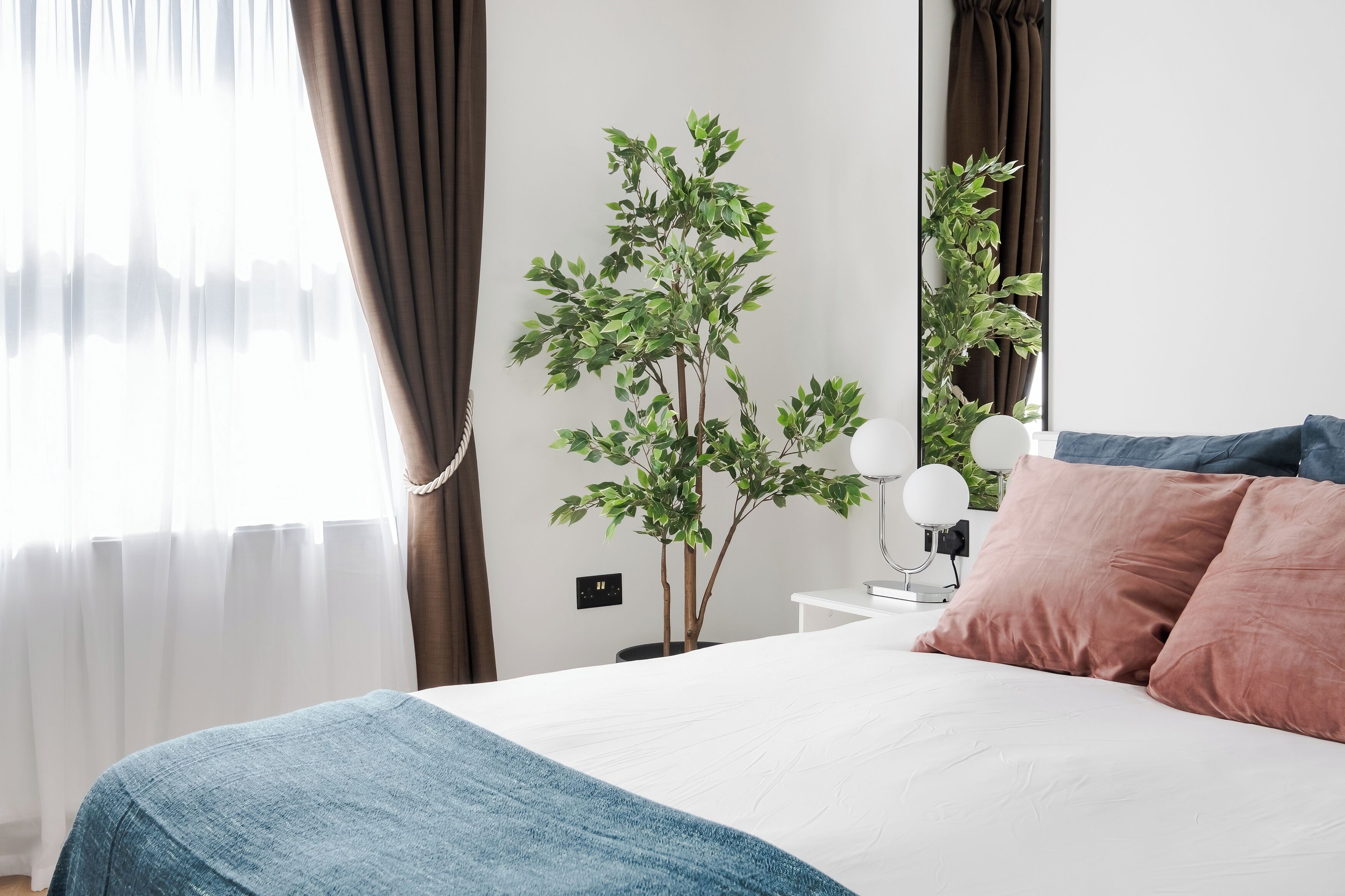 Une chambre à coucher avec un lit, une table de chevet avec une lampe, une plante en pot et une fenêtre avec des rideaux.