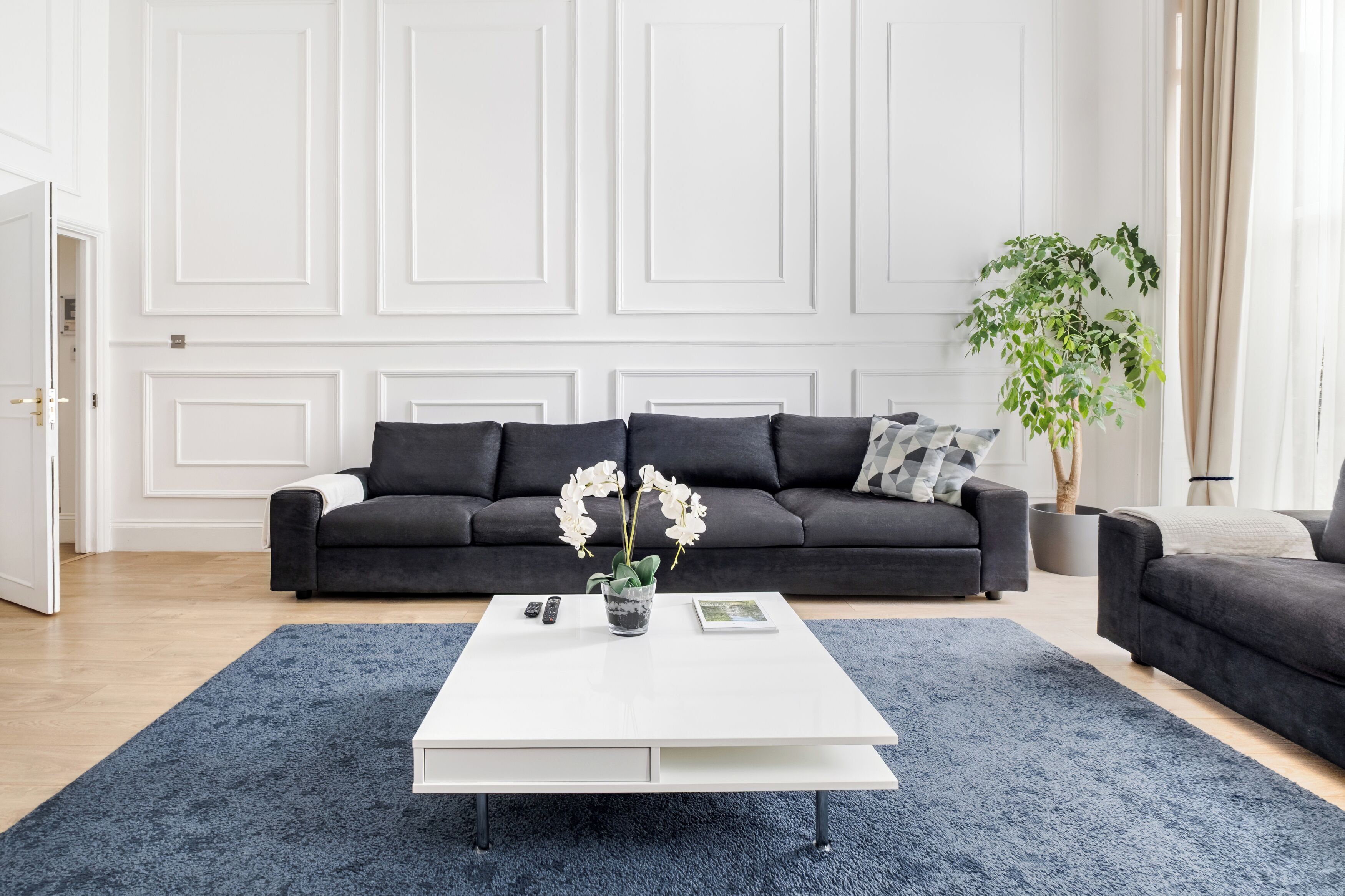 A modern living room with a dark grey sofa, a white coffee table, and a blue rug.