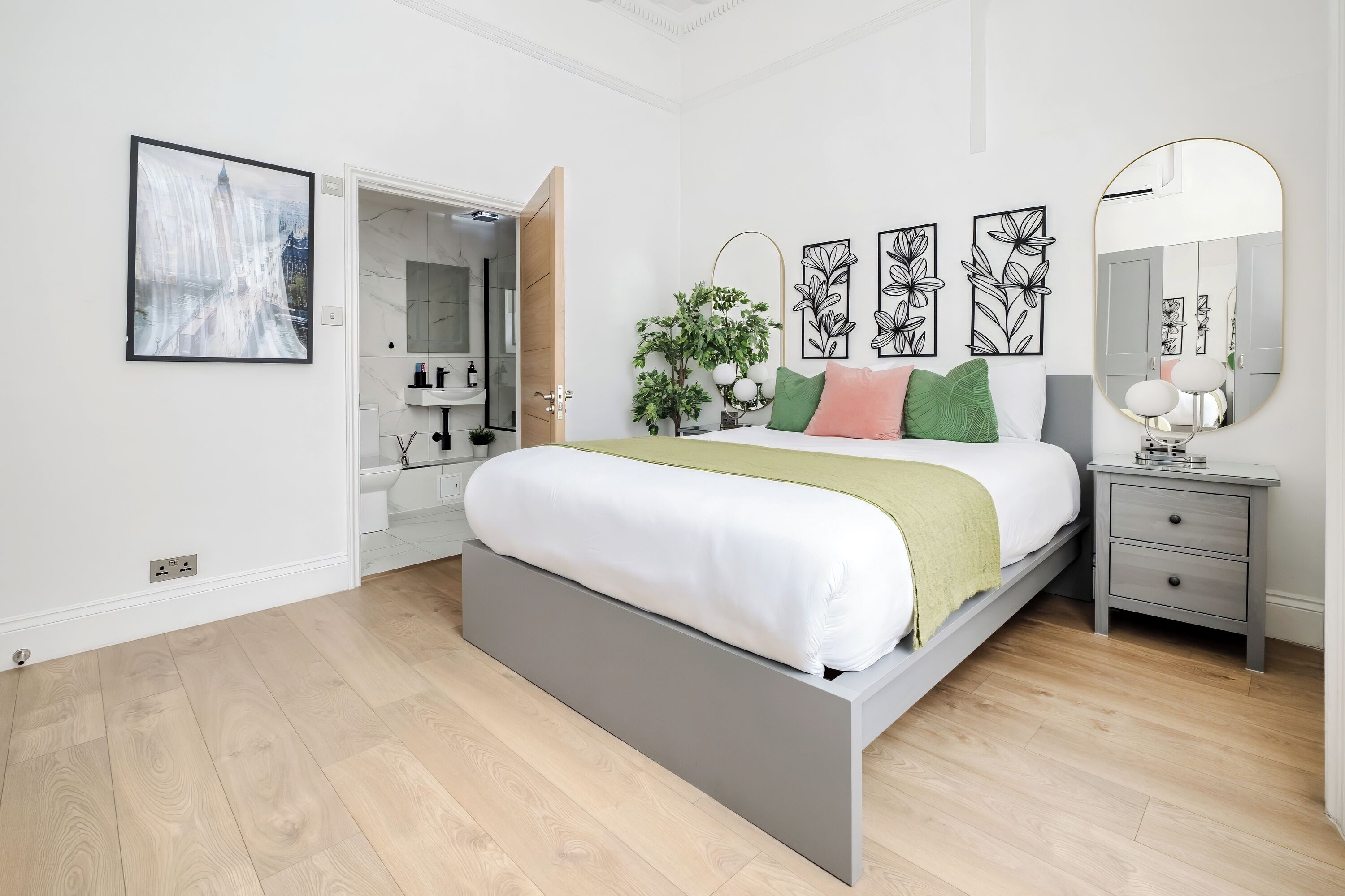 A modern bedroom with a bed, bedside tables, a mirror, and artwork on the walls.