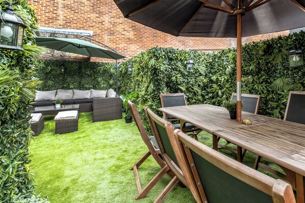 A patio with a wooden table and chairs, a sofa, and an umbrella.