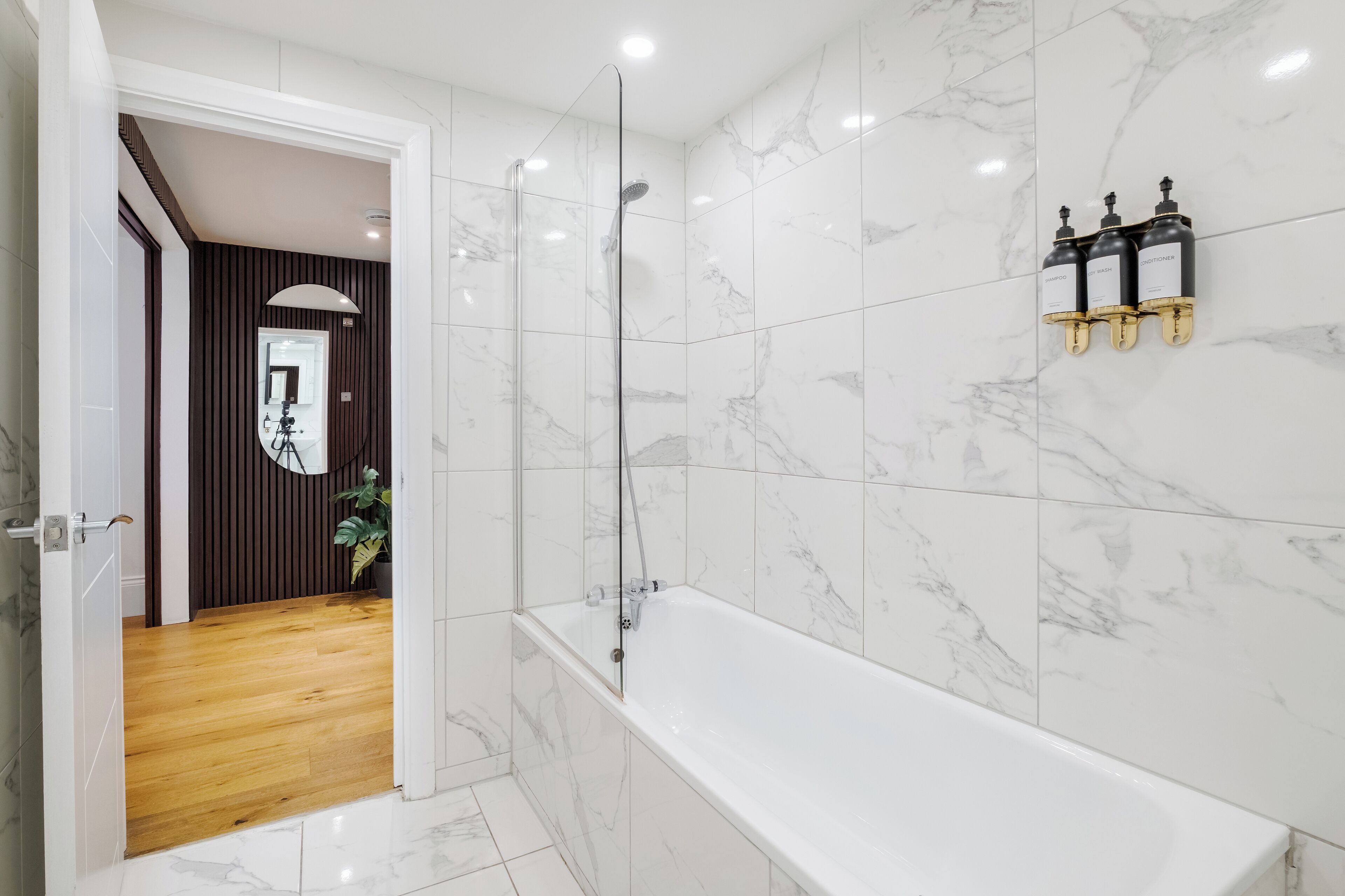 A modern bathroom with a glass-enclosed shower, a white bathtub, and marble walls.